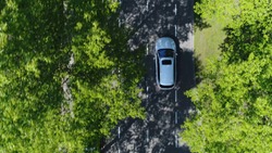 Aerial top down view of grey station wagon vehicle overtaking drone camera driving over straight road testing area for development of self driving electronic automobiles ev's 4k high resolution