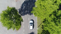 Aerial following car top-down view this grey colored station wagon is driving over two way street with green trees on both sides of street