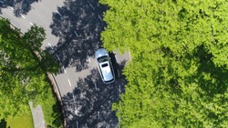 Aerial following car top-down view this grey colored station wagon is driving over two way street corner green trees on both sides of street