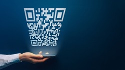 Qr code payment concept. Hand holding mobile smart phone with qr code for payment pay, scan barcode technology on dark background. Online shopping, cashless society symbol. Copy space.