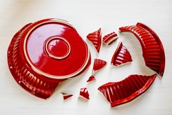 Shards of broken red kitchen utensils. Trying to glue pieces together is unsolvable task. Broken ceramic plate top view. Broken relationship, broken heart, family discord