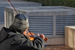 homeless violonist plays on the street on a sunny winter say