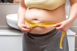 Midsection of an obese woman measuring her waist with a measuring tape in the bathroom