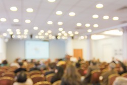 Blurred image of audience people in hall or auditorium with screen, blur background