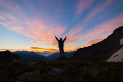 Man standing on mountain top outstretching arms, sunrise light colorful sky scenis landscape, conquering success leader concept.