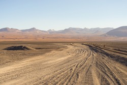 Dirt road at high altitude with sandy desert and barren volcano range on the Andean highlands. Road trip to the famous Uyuni Salt Flat, among the most important travel destination in Bolivia.