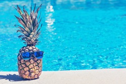 Funny pineapple in sunglasses near swimming pool.