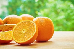 Orange, half of orange, orange lobule and basket with oranges on the wooden table on the green blurred background
