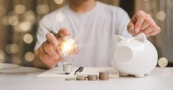 business man hand holding lightbulb and putting coin in to the piggy bank. idea saving energy and accounting finance in home and family concept, save world and energy power.