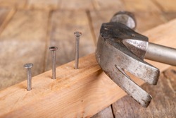Carpenter's hammer and steel nails on a wooden workshop table. Small carpentry work in the workshop. Dark background.