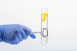 Test tube with yellow reagent and pipette close-up. Colored liquid in test tube in hand. Yellow liquid drop from glass pipette to test tube, isolated on white .