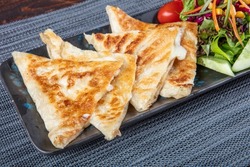 Gozleme is Turkish pastry. Freshly baked appetizing Turkish tortillas Gozleme with with feta cheese on a wooden board and with turkish tea. Space for text. Handmade Turkish traditional pastries.