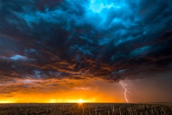 A nighttime, tornadic mezocyclone lightning storm shoots bolt of electricity to the ground and lights up the field and dirt road in Tornado Alley.