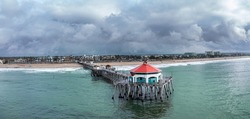 Aerial view of famous Huntington Beach pier in Orange County California shows the beautiful platform jutting out over the green, cool water frames against a stormy black sky.
