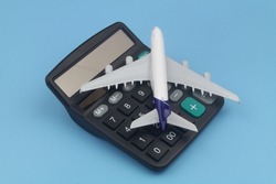Airplane tickets price, travel budget, cost or expenses concept. Airplane model and calculator on blue background.