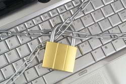 Cyber safety concept. Locked chain by padlock on silver laptop computer keyboard.