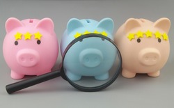 Financial organizations ranking. Magnifying glass and piggy banks with yellow stars on gray background.