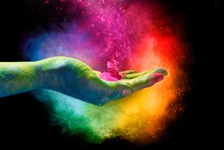 Holi festival concept. Magical rainbow colored powder exploding from the palm of a cupped hand creating a vibrant cloud of dust in the colors of the spectrum over a black background.
