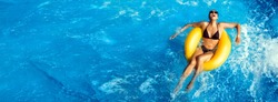 Summer vacation, Laughing young woman enjoying an aqua park with a yellow float on sparkling blue water in a pool with turbulence and copy space in an overhead panorama