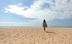 Woman walking away in the distance across a sandy tropical beach to the sea on a sunny spring or summer day with copy space in a vacation or travel concept