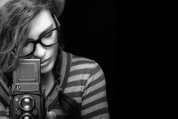 Female photographer. Close up Attractive Young Woman in Trendy Outfit Capturing Photo Using Vintage Camera. Black and White Portrait Isolated on Black Background with Copy Space.