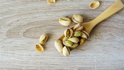 Pistachio nuts are in a wooden spoon placed on a wooden table.