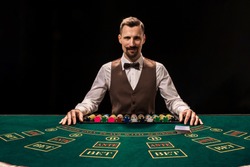 Portrait of a croupier is holding playing cards, gambling chips on table. Black background
