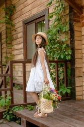 Dark-haired tween girl standing on wooden doorstep with basket of wildflowers