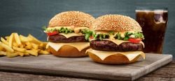Two craft beef burgers on wooden table on blue background.