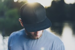 Photo Bearded Young Man Wearing Black Blank Cap. Green City Park Lake Background and Sunset effect. Front view. Horizontal Mockup.