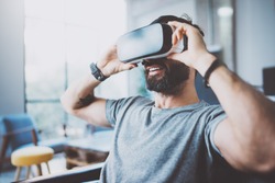 Bearded man wearing virtual reality goggles in modern coworking studio. Smartphone using with VR headset. Horizontal, blurred