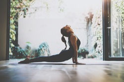 Portrait of gorgeous young woman practicing yoga indoor. Beautiful girl practice cobra asana in class.Calmness and relax, female happiness.Horizontal, blurred background.Visual effects