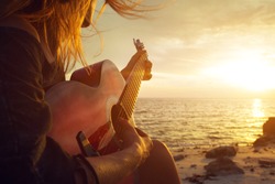 Woman playing guitar on sunset beach