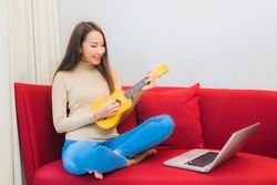Portrait beautiful young asian woman play ukulele on sofa in living room interior