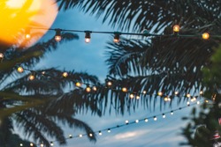 blurred light bokeh with coconut palm tree background on sunset, yellow string lights with bokeh decor in outdoor restaurant