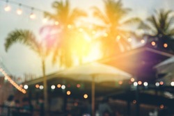 blurred bokeh light on sunset with yellow string lights decor in beach restaurant 