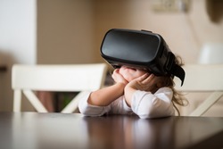 Child with virtual reality headset sitting behind table indoors at home