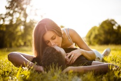 Young multi racial couple kissing in nature on grass - woman lies on man