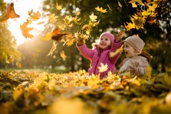 Siblings playing with maple leaves in autumn park