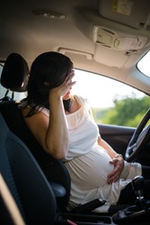 Young pregnant woman behind the car steering wheel having problems