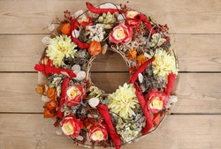 Door wreath made of artificial flowers on wooden background