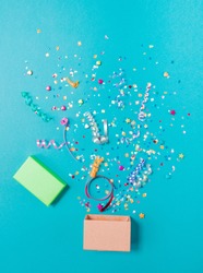 Pink gift box with various party confetti, streamers, noisemakers and decoration on a blue background. Colorful celebration concept.