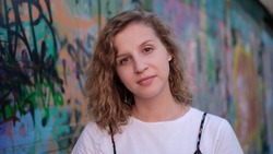 Portrait of a cute curly woman looking at the camera against a graffiti wall. Deep gaze.