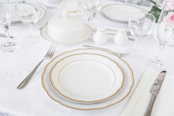 Beautifully decorated table with empty white plates, glasses, cutlery and flowers on luxurious tablecloths