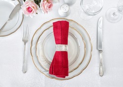 Beautifully decorated table with white plates, glasses, antique cutlery and red napkin are on luxurious tablecloths