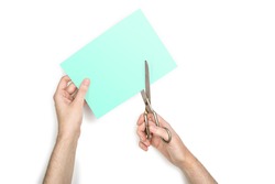 A woman is cutting a sheet of green paper using  metallic scissors, isolated on white background