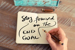 Retro effect and toned image of a woman hand writing a note with a fountain pen on a notebook. Handwritten text STAY FOCUSED ON THE END GOAL, business success concept