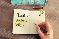 Retro effect and toned image of a woman hand writing a note with a fountain pen on a notebook. Handwritten text CREATE AN ACTION PLAN next to yellow lighting bulb as symbol for bright idea.