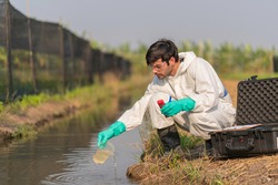 A technician in full body protective suit collecting sample of water ,Portable water quality measurement ,water quality for agriculture ,ph checking on field