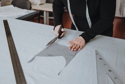 Tailor designer working of cutting piece of cloth with scissors, a triangle and a ruler lie on the table nearby, entrepreneur concept.